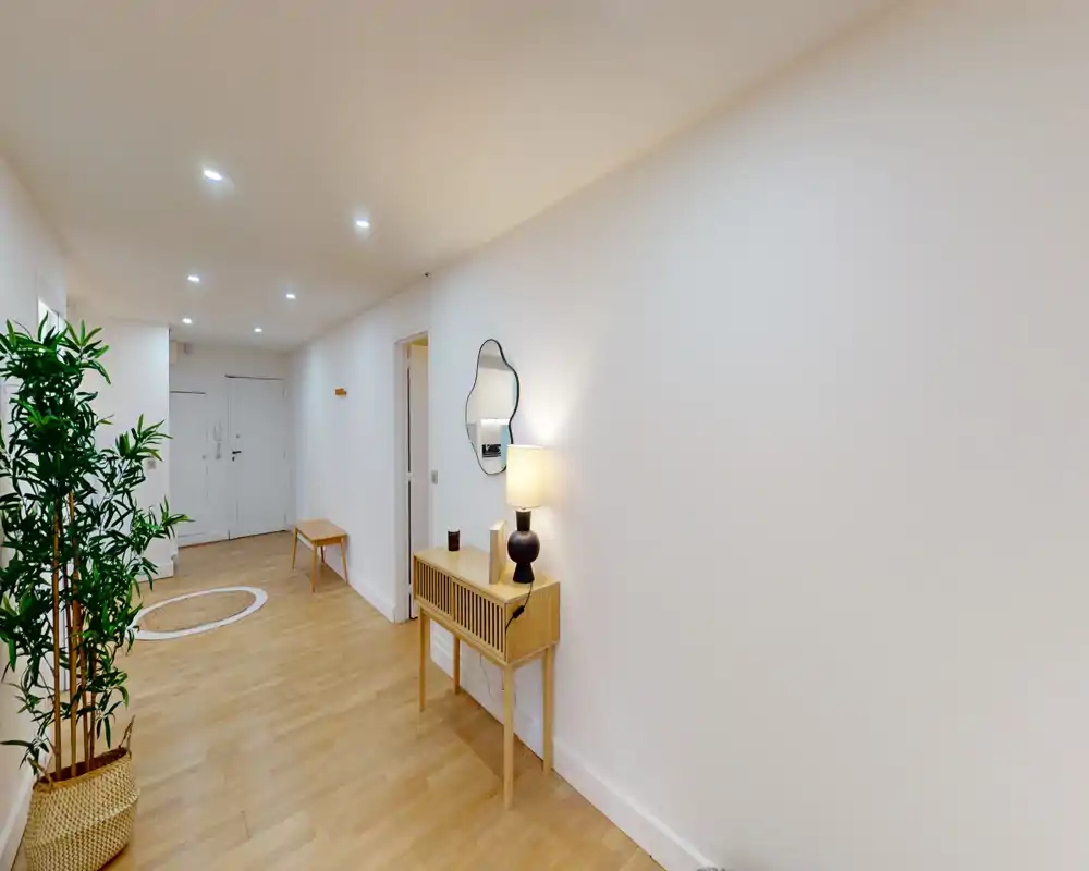 Bright, modern entry hallway with wooden flooring, a console table with lamp and mirror, and a potted plant — welcoming and neatly styled.