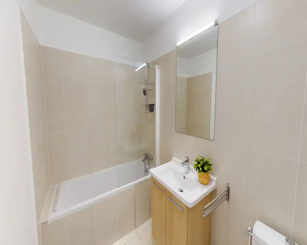 Modern tiled bathroom with bathtub, glass shower screen, wall-mounted mirror and a compact sink cabinet; bright, clean and minimal.