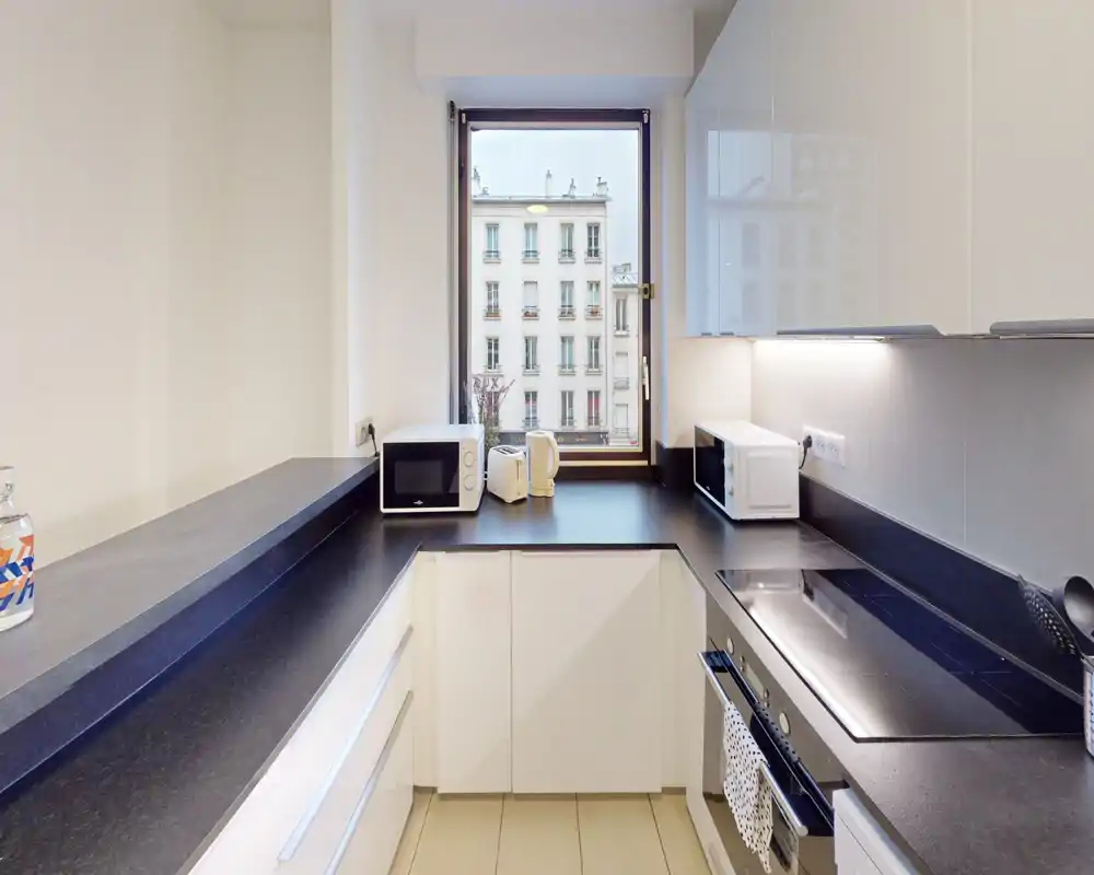Bright modern kitchenette with black countertops, integrated stovetop, and small appliances (microwave, kettle). A compact, well-lit space ideal for short stays.
