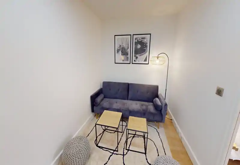 Small, cozy living area with a plush two-seater sofa, patterned rug, two nesting coffee tables and warm floor lamp — ideal for relaxing in a compact space.