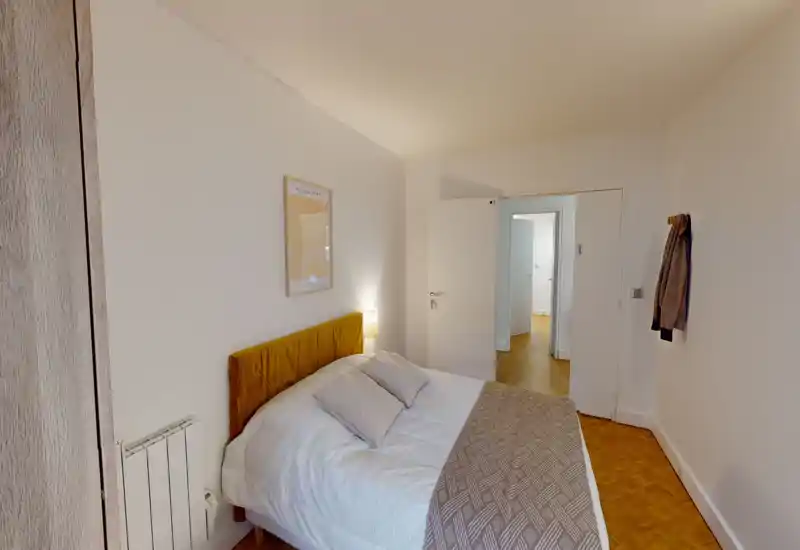 Bright, neatly styled bedroom with a comfortable double bed, warm headboard and bedside lamp, neutral walls and wooden parquet flooring.