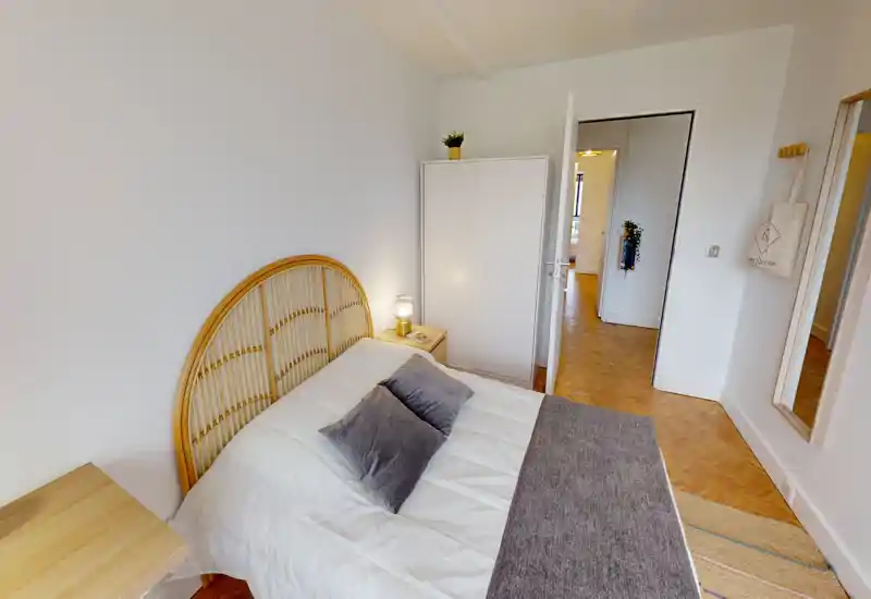 Bright, well-styled bedroom with a rattan headboard, comfortable double bed, bedside table with lamp and a wardrobe — ideal for a cozy stay.