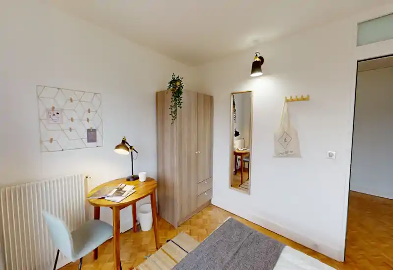 Bright, neatly styled bedroom corner with a small wooden wardrobe, desk and a partially visible bed with cozy textiles — ideal for a single occupant.