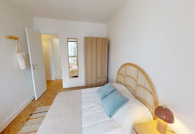 Camera da letto luminosa e accogliente con testiera in rattan, due cuscini turchesi e lampada da comodino — perfetta per un soggiorno rilassante.