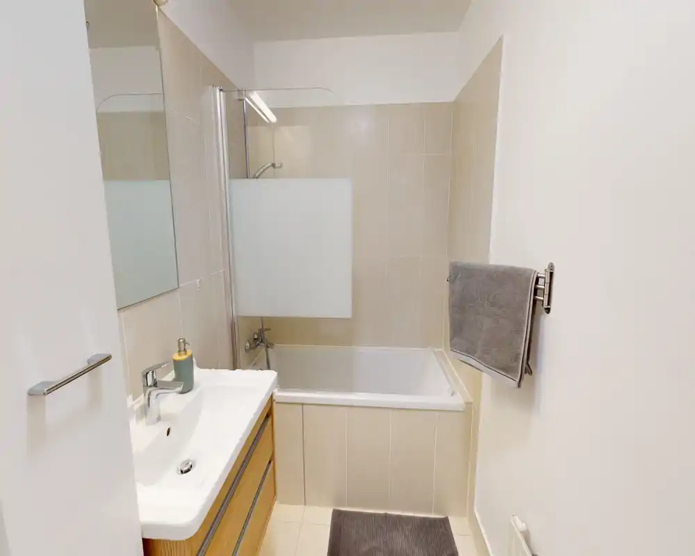 Clean, modern bathroom with a bathtub and shower screen, a wall-mounted towel rail and a vanity with sink and mirror.