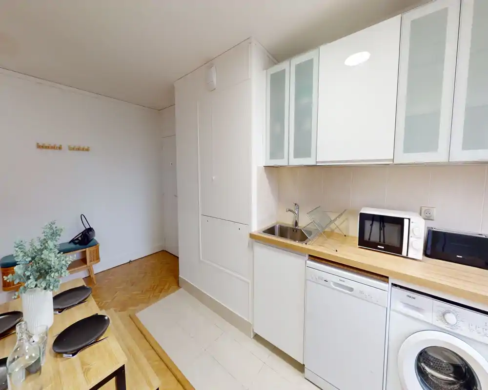 Bright, compact kitchenette with a wooden countertop, sink, microwave and washer-dishwasher units — ideal for a studio apartment.