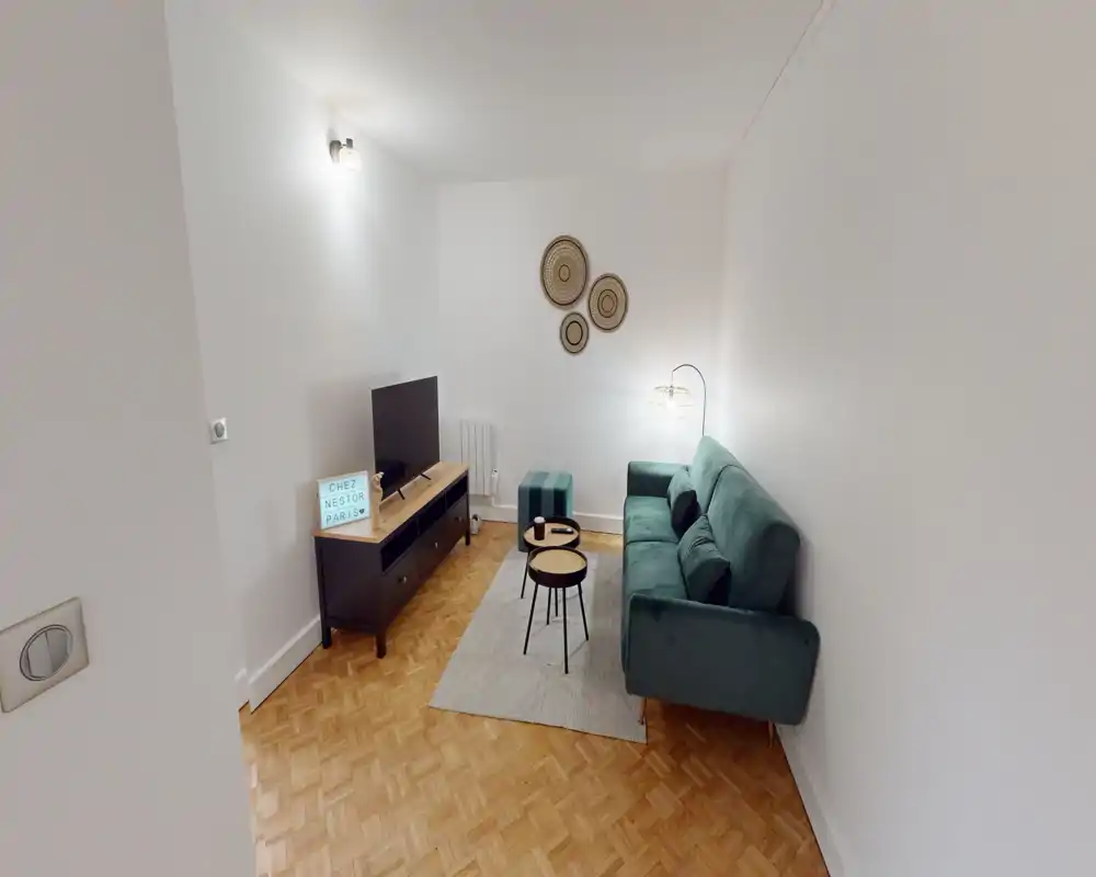 Compact, well-staged living room with a green sofa, small nesting coffee tables, TV console and soft lighting—comfortable and modern for a city apartment.
