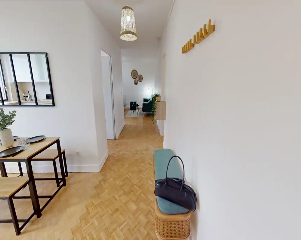 Bright, tidy entrance/hallway leading into an open-plan living and dining area. The space features parquet flooring, a small bench with coat hooks and a view through to a sofa and dining table.