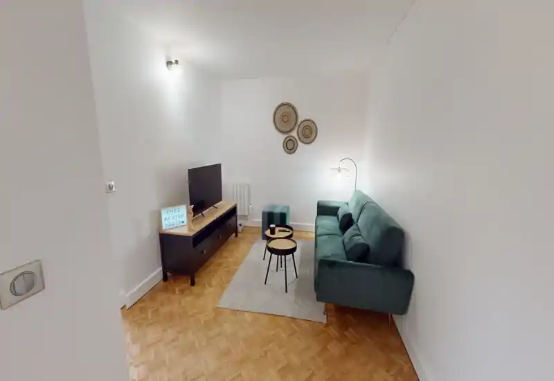 Compact, well-staged living room with a green sofa, small nesting coffee tables, TV console and soft lighting—comfortable and modern for a city apartment.