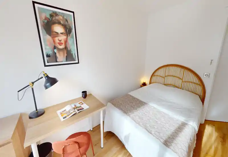 Chambre simple lumineuse et chaleureuse avec tête de lit en rotin, lit bien fait et petit bureau en bois idéal pour travailler ou lire.