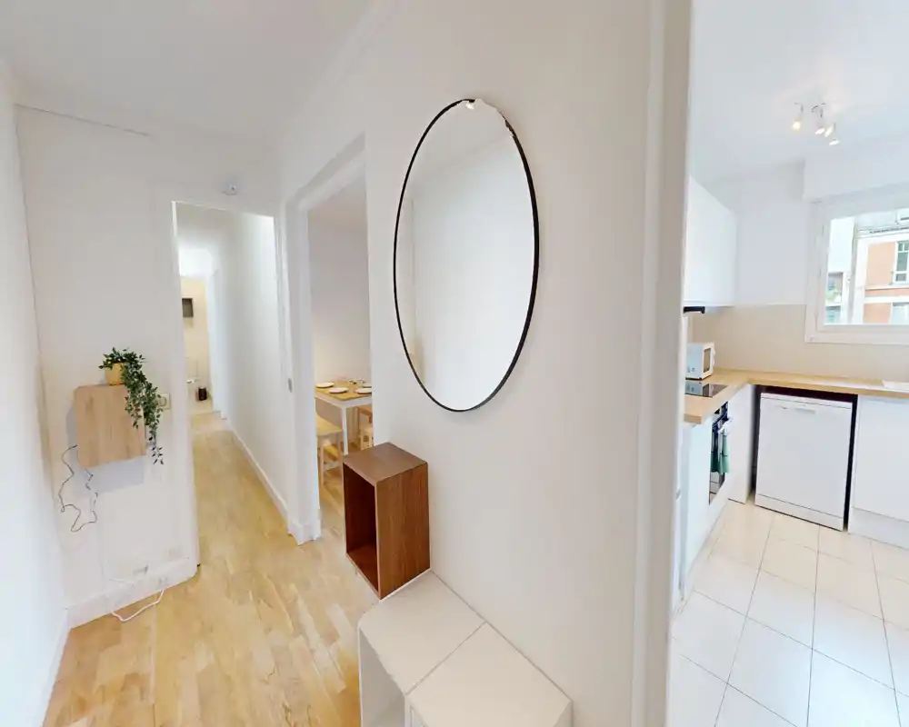 Entrée d'appartement lumineuse avec parquet clair, grand miroir rond et petit meuble console — espace d'accueil propre et moderne reliant la cuisine et la salle à manger.