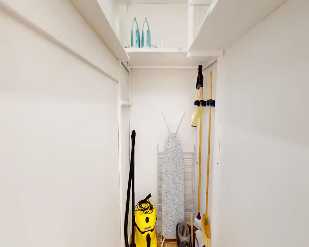 Placard utilitaire/rouchoir avec aspirateur, planche à repasser, balais et étagères — petit espace de rangement pour le matériel de nettoyage.