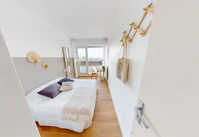 Chambre lumineuse et moderne avec grand lit, linge de lit douillet, coussins décoratifs et un petit bureau près de la fenêtre offrant une vue sur la ville.