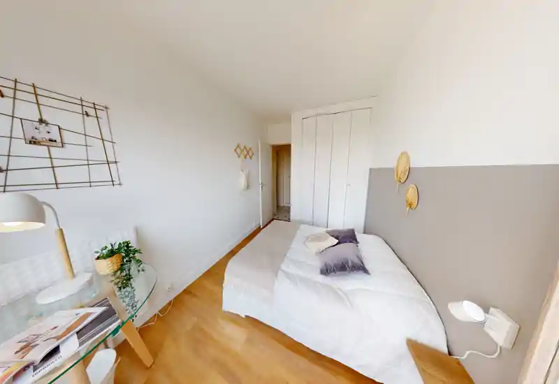 Chambre lumineuse et bien mise en scène avec lit double, coussins moelleux et sol en bois chaleureux; murs blancs et placard intégré pour une ambiance moderne et apaisante.