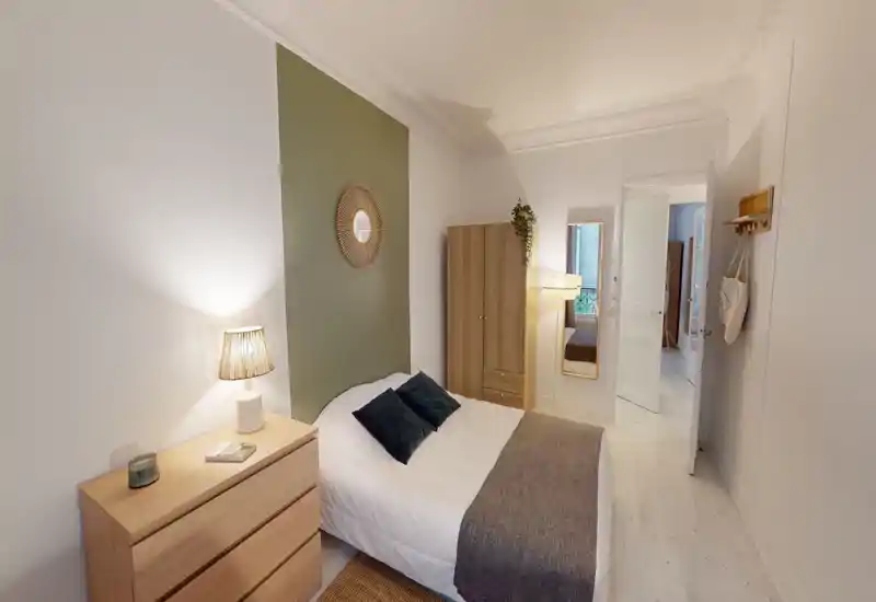 Bright, styled bedroom with a double bed, bedside lamp, chest of drawers and a wardrobe; calming green accent wall and soft textiles create a cozy atmosphere.