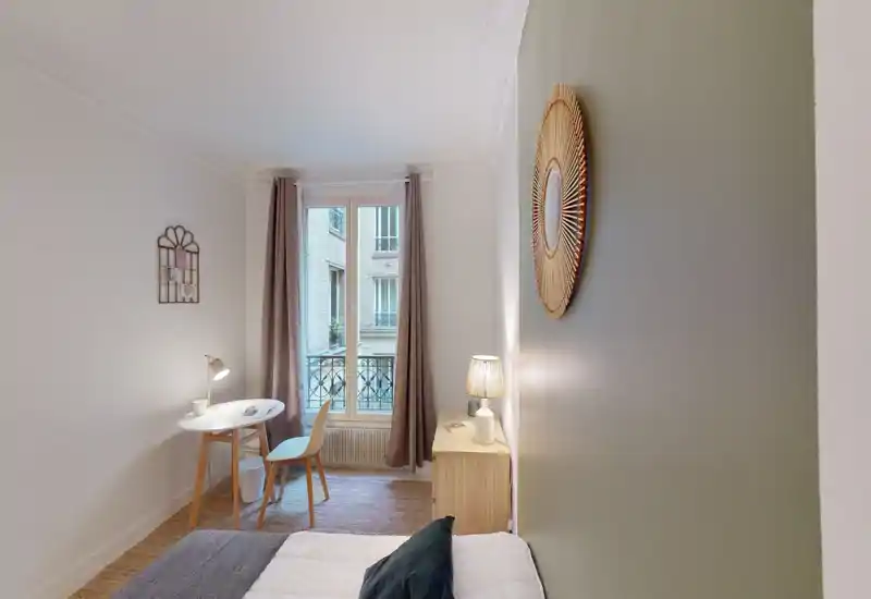 Bright, neatly styled bedroom with a single bed, bedside table and a small desk by the window — ideal for a cozy city stay.