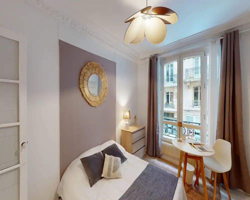 Bright, stylish bedroom with a comfortable double bed, decorative cushions, a bedside lamp, and a small table by the window letting in natural light.