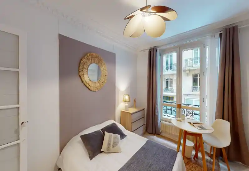 Bright, stylish bedroom with a comfortable double bed, decorative cushions, a bedside lamp, and a small table by the window letting in natural light.