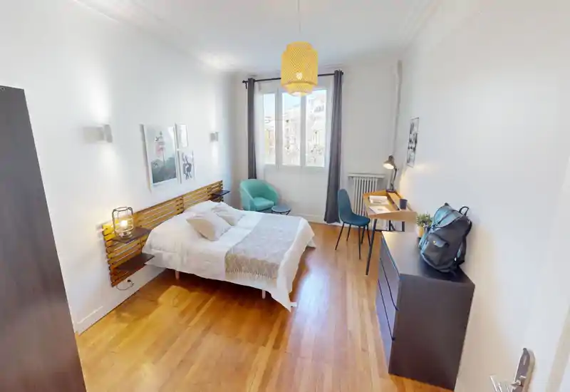 Bright, well-staged bedroom with a double bed, cozy textiles and a small seating area by the window. Hardwood floor and a desk create a practical, inviting space ideal for rentals.