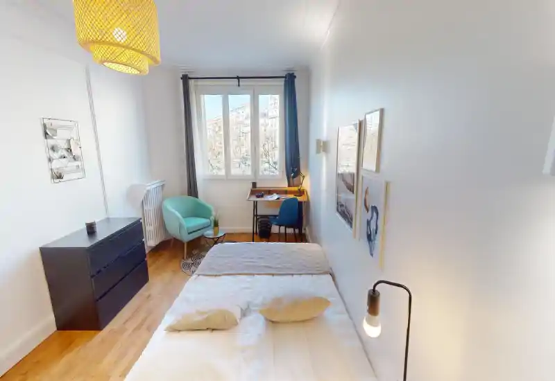 Camera da letto luminosa e ben arredata con un letto matrimoniale in primo piano, una piccola postazione di lavoro vicino alla finestra e una poltrona accogliente. La luce naturale e il pavimento in legno creano un ambiente invitante.