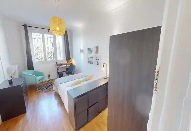 Camera da letto luminosa e arredata con letto matrimoniale, lampade da comodino, una scrivania vicino alla finestra e una poltrona confortevole. La grande finestra regala molta luce naturale e il pavimento in legno rende l’ambiente accogliente.
