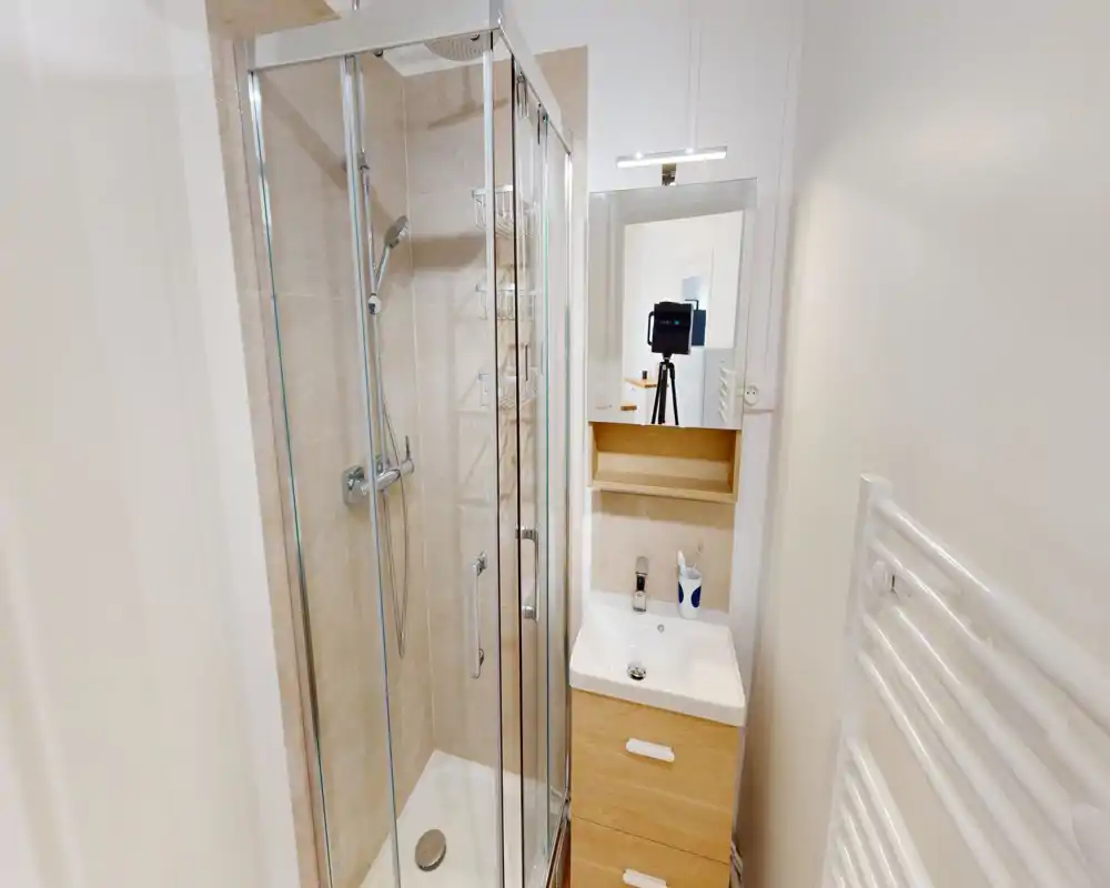 Bagno compatto e moderno con cabina doccia in vetro, miscelatore a parete, piccolo mobile lavabo con specchio e scaldasalviette.