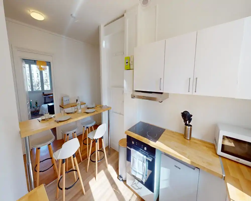 Cucina compatta e luminosa con piani in legno, piano a induzione, forno integrato e bancone colazione con sgabelli — perfetta per un appartamento cittadino accogliente.
