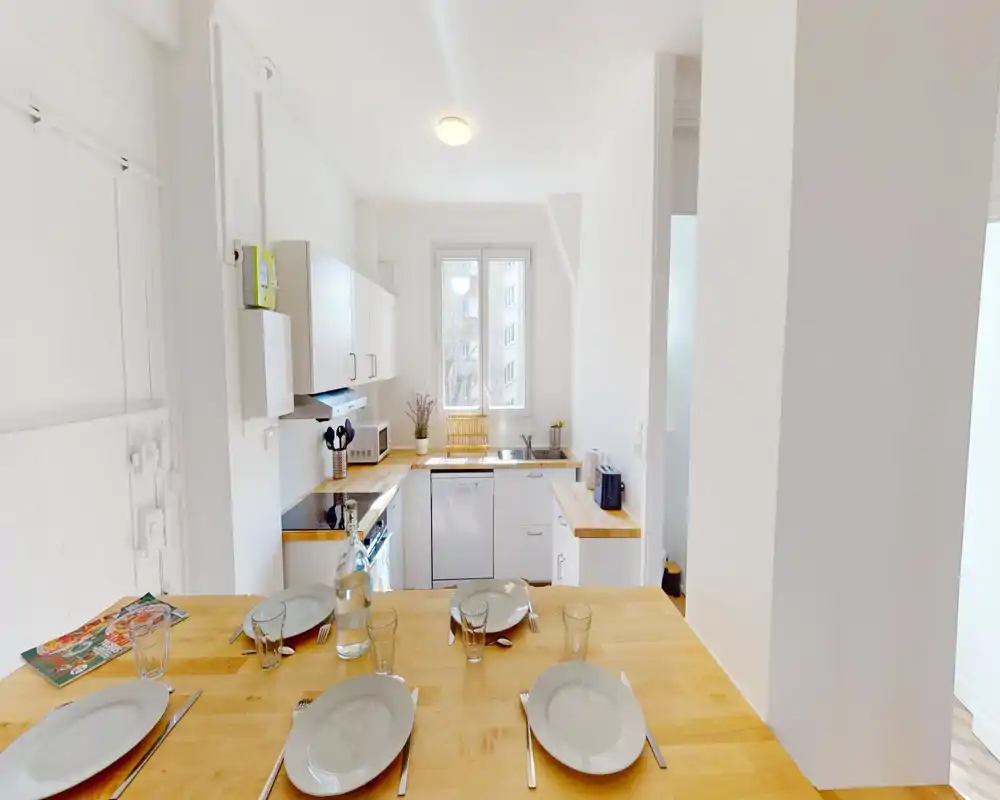 Cucina moderna e luminosa con piani in legno, elettrodomestici integrati e tavolo per quattro, perfetta per un appartamento compatto.