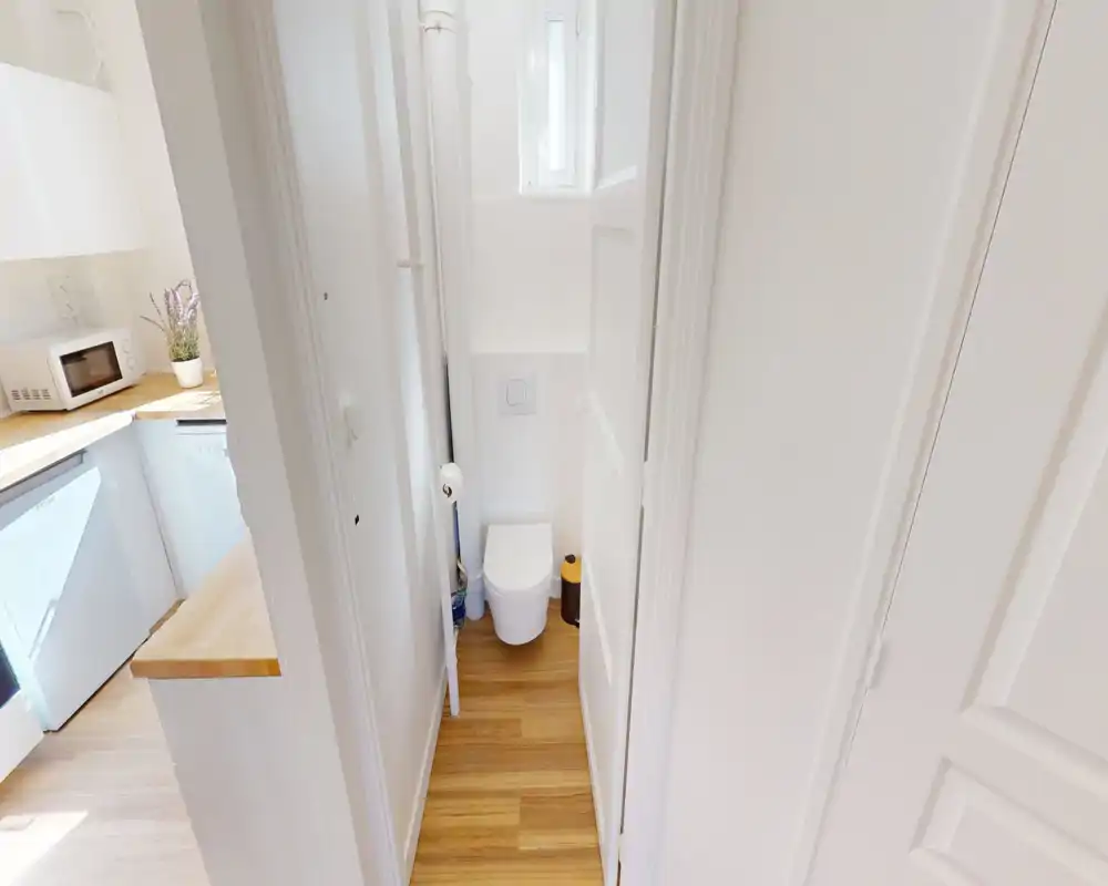 WC compatto e ben illuminato con wc sospeso e pavimento in legno. Lo spazio stretto è pulito e luminoso, ideale come bagno per gli ospiti.