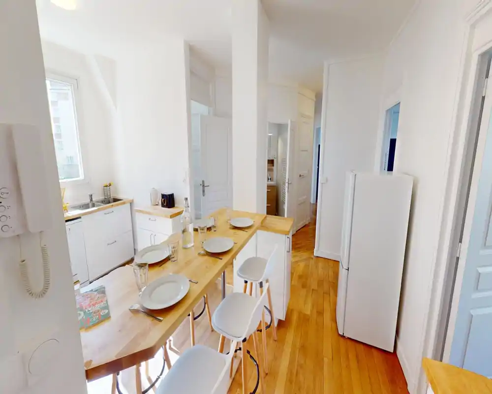 Cucina moderna e luminosa con bancone in legno apparecchiato per quattro, mobili bianchi e frigorifero — ambiente accogliente e ben illuminato ideale per pasti informali.