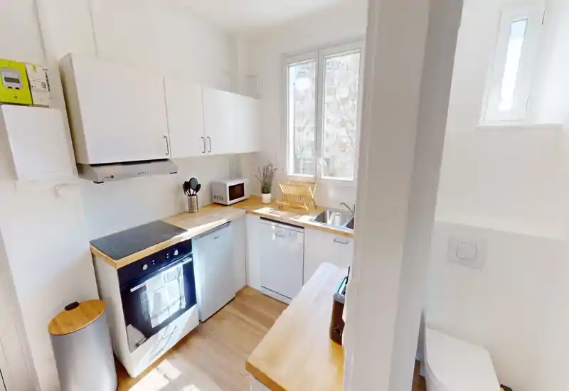 Compact, bright kitchen with white cabinets, wooden countertops, electric stove, dishwasher and a sink by the window — ideal for a small apartment.
