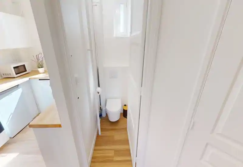 Compact, well-lit WC with a wall-mounted toilet and wooden flooring. The narrow space is clean and bright, ideal for a guest toilet.