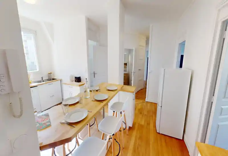 Bright modern kitchen with a wooden breakfast bar set for four, white cabinets and a refrigerator — a cozy, well-lit space ideal for casual meals.