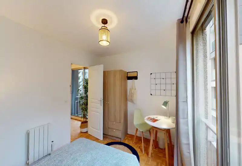 Camera da letto luminosa e ordinata con letto parzialmente visibile, armadio e piccola scrivania vicino alla finestra—ideale per una persona o una coppia.