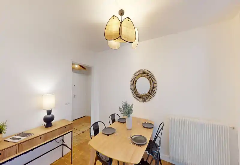 Zona pranzo luminosa e di stile con tavolo in legno per quattro persone, specchio decorativo e lampada a sospensione calda — perfetta per pranzi accoglienti.