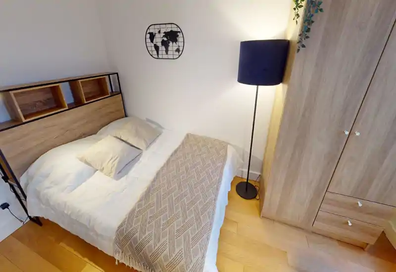 Well-styled bedroom with a double bed, neutral linens, a patterned throw and a wardrobe; warm wood tones and soft lighting create a cozy atmosphere.