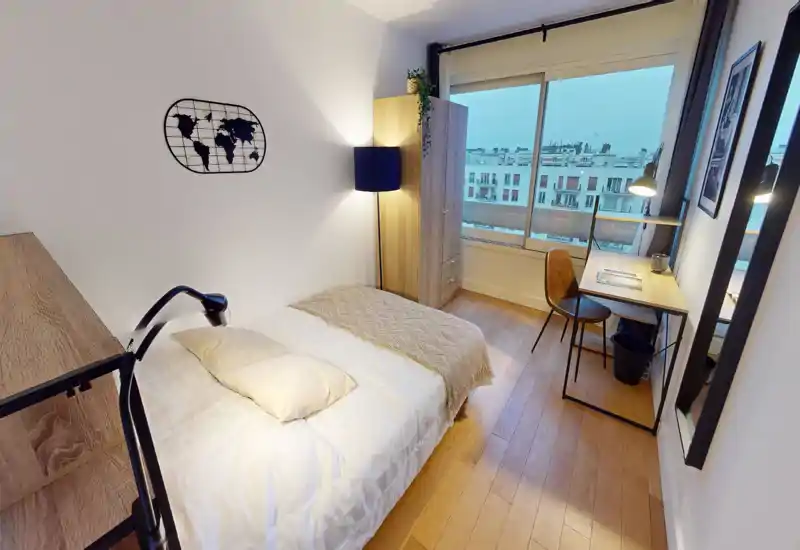 Bright, well-staged single bedroom with a comfortable-looking bed, wooden flooring, wardrobe and a desk by a large window offering city views.