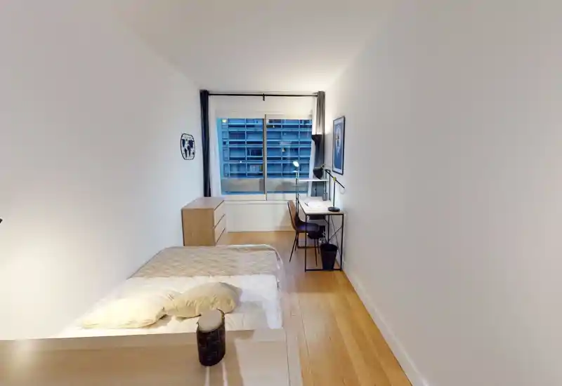 Camera da letto luminosa e compatta con letto singolo ben rifatto, pavimento in legno chiaro, comò e una piccola scrivania vicino alla finestra — ideale per uno studente o single.