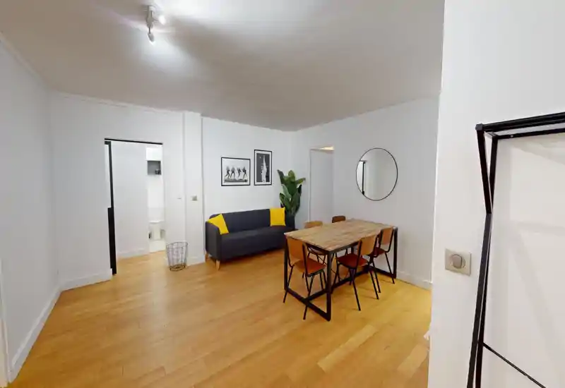 Soggiorno moderno e luminoso con divano grigio e cuscini gialli, tavolo da pranzo in legno con sedie, quadri alle pareti e specchio rotondo — perfetto per pranzi informali e momenti conviviali.