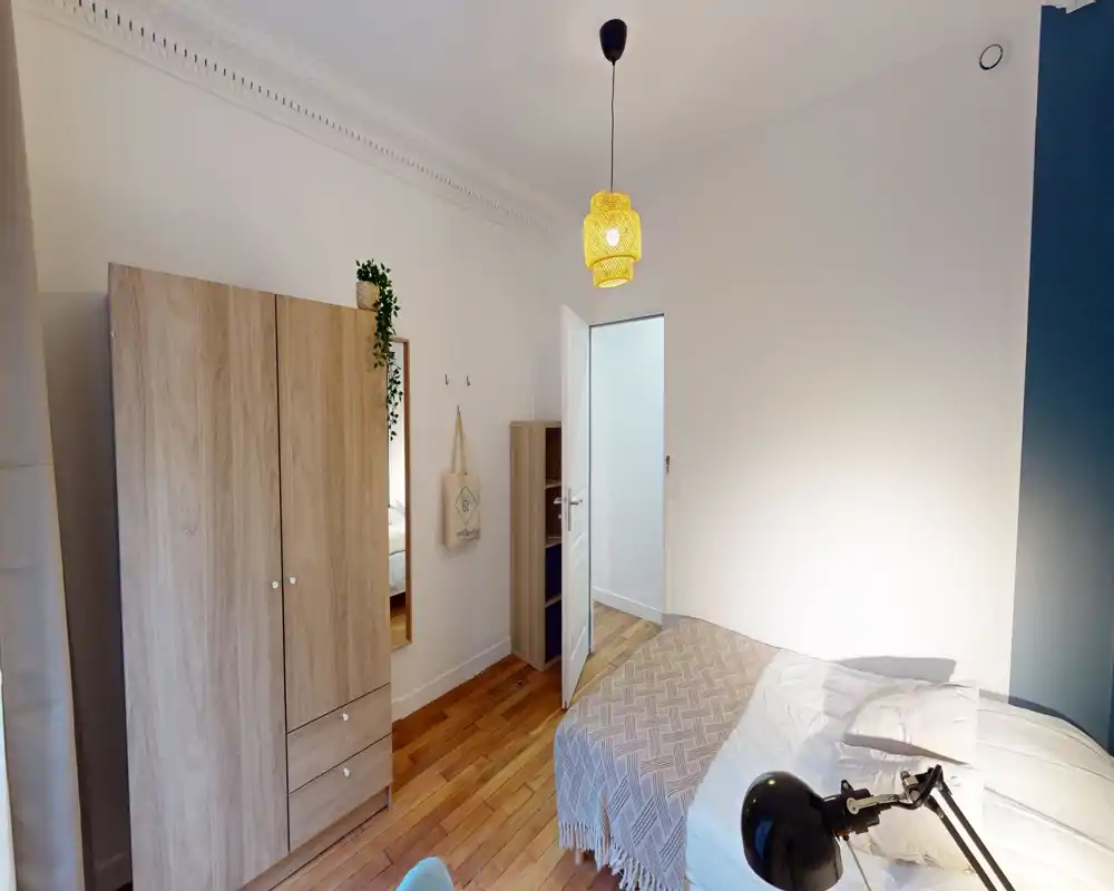 Chambre lumineuse et bien aménagée avec un lit double confortable, parquet chaleureux et une armoire. L'atmosphère est cosy grâce aux textiles et à la suspension, idéale pour une annonce locative.