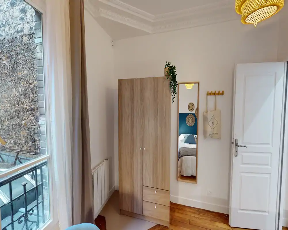 Coin chambre lumineux et bien aménagé avec une armoire et une grande glace reflétant le lit; une grande fenêtre apporte une belle lumière naturelle et le sol en bois réchauffe l'ambiance.