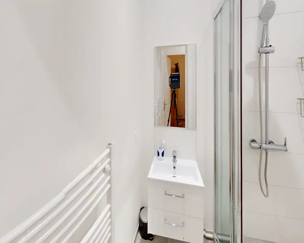 Petite salle de bain moderne avec cabine de douche, meuble-lavabo mural et sèche-serviettes. Carrelage blanc et robinetterie chromée pour un style propre et minimaliste.
