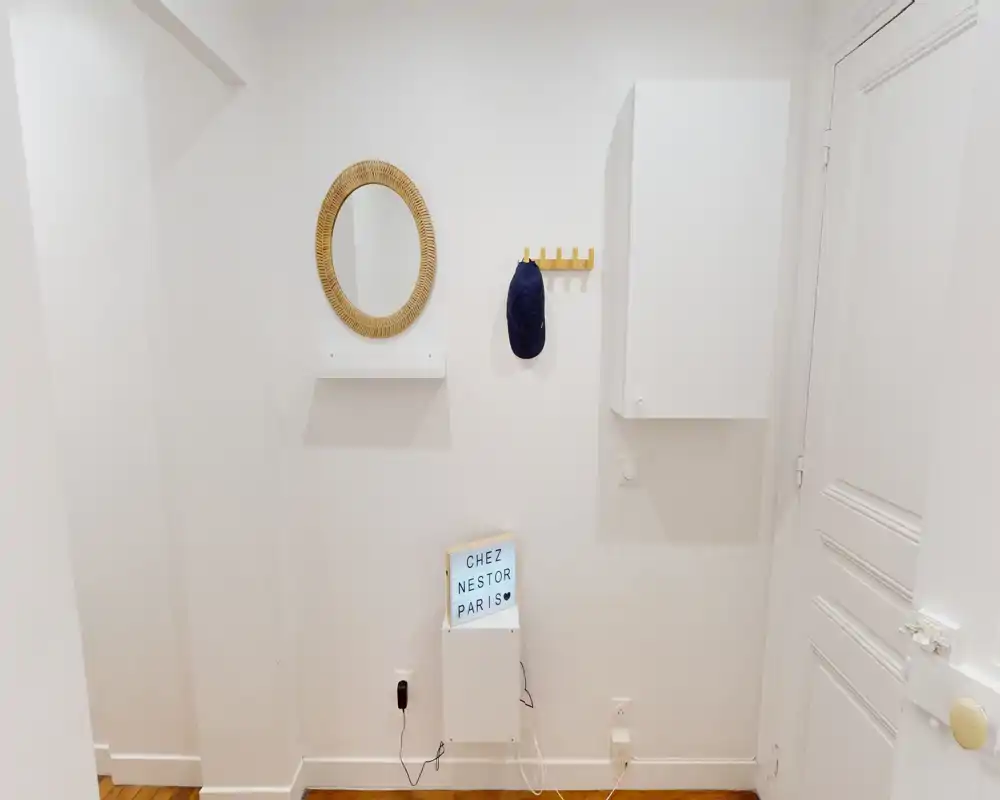 Petit hall d'entrée lumineux avec miroir rond, patères et meuble mural compact — décor minimaliste et soigné, idéal pour une location.