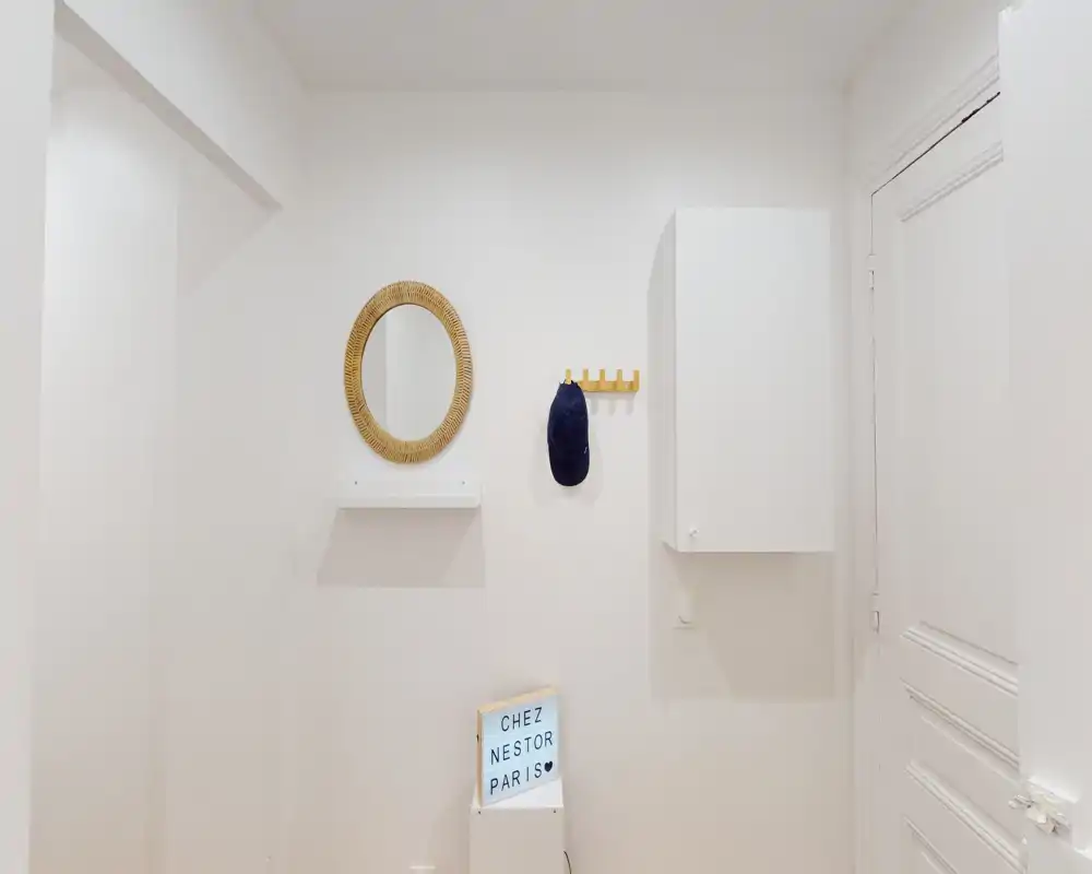 Entrée minimaliste et lumineuse avec miroir mural, petite étagère, crochets et placard — vestibule propre et accueillant.