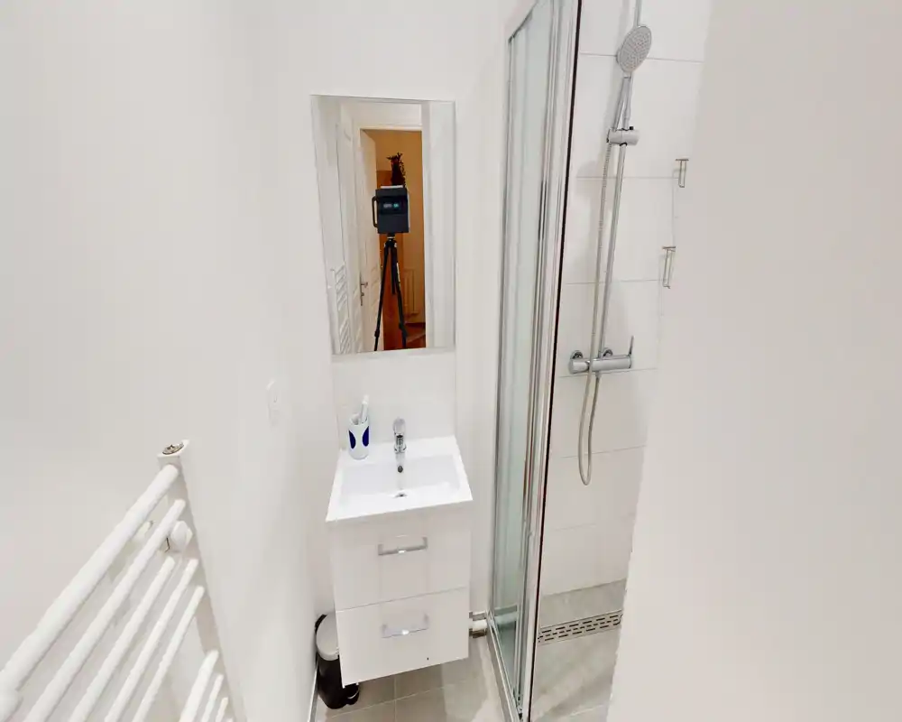 Salle de bains compacte et moderne avec meuble vasque, miroir et douche vitrée; carrelage blanc et bonne luminosité pour un rendu propre.