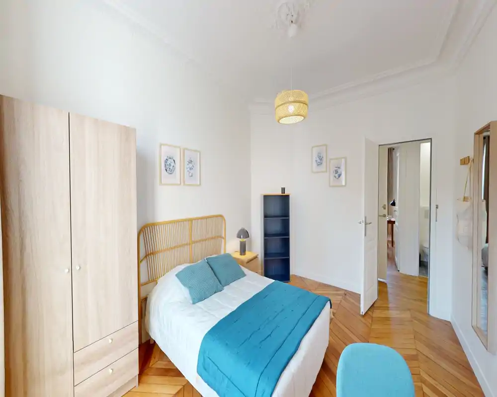 Chambre lumineuse et chaleureuse avec tête de lit en rotin, jeté et coussins bleu-vert, armoire en bois et parquet — un espace nuit accueillant.