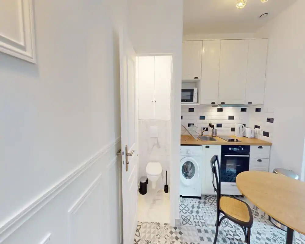 Cucinotto compatto e di stile con piano in legno, mobili bianchi, forno integrato e lavatrice; piastrelle a motivi e un piccolo tavolo da pranzo rendono lo spazio pratico e accogliente.