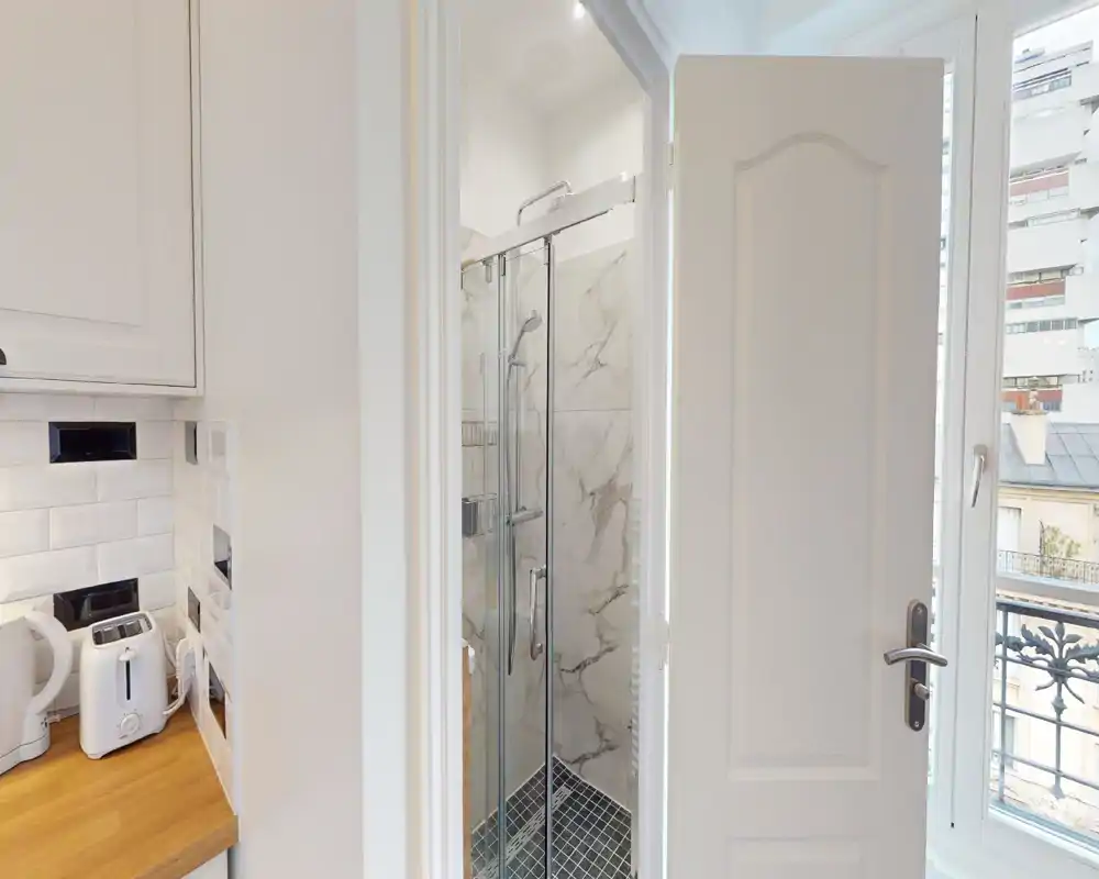 Bagno moderno e compatto con cabina doccia in vetro, piastrelle effetto marmo e piatto doccia piastrellato; luce naturale luminosa dalla finestra adiacente.