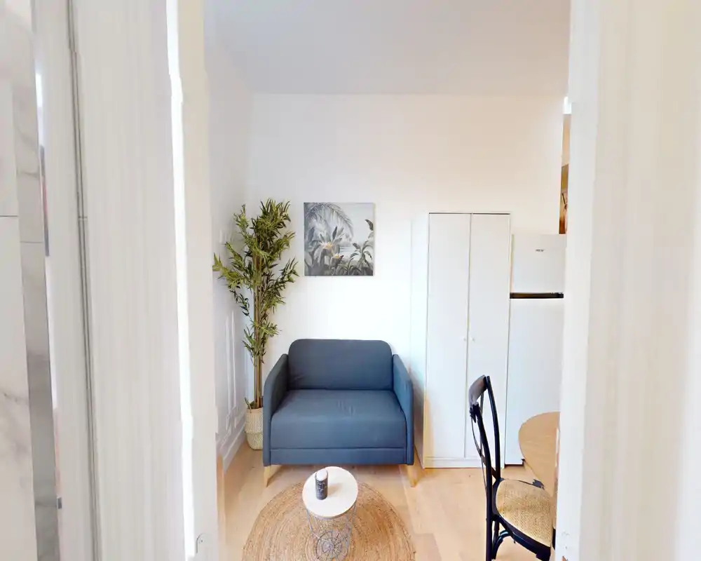 Zona giorno luminosa e ben arredata con un divano due posti compatto, tappeto intrecciato e tavolino: pianta e quadro a parete rendono l'ambiente accogliente.