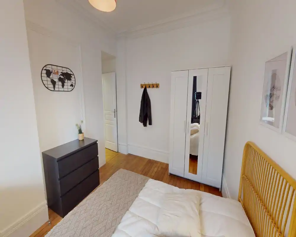 Camera da letto luminosa e dallo stile semplice, con letto parzialmente visibile, testiera in legno e armadio con specchio; pavimento in legno e arredi minimal creano un ambiente tranquillo.